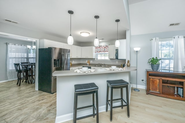 kitchen with stainless steel fridge, white cabinetry, decorative light fixtures, and light wood-type flooring