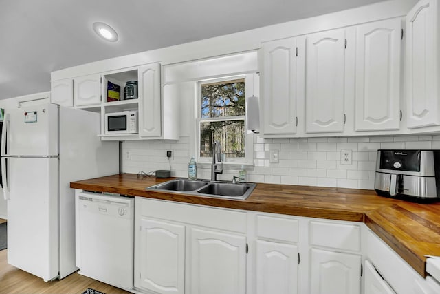 kitchen with backsplash, white appliances, white cabinetry, wood counters, and a sink