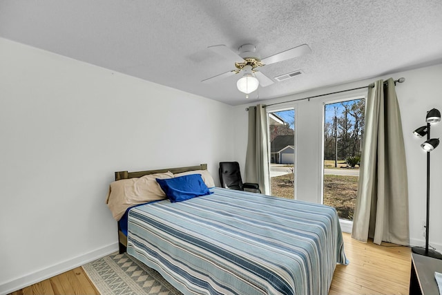 bedroom featuring baseboards, visible vents, light wood finished floors, ceiling fan, and a textured ceiling