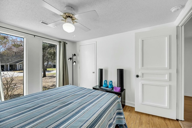 bedroom featuring visible vents, a textured ceiling, light wood finished floors, baseboards, and ceiling fan