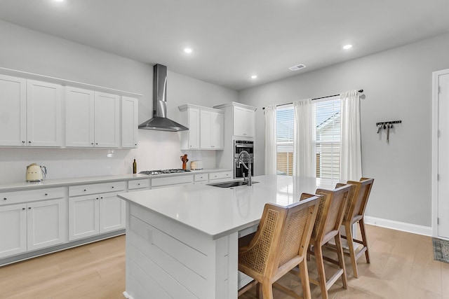 1017 Marsh Royal St, Summerville, SC 29485 - kitchen featuring wall chimney exhaust hood, a sink, light wood finished floors, a breakfast bar, and a kitchen island with sink