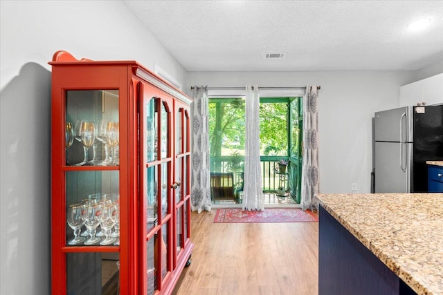interior space with a textured ceiling, light wood-type flooring, light stone countertops, visible vents, and freestanding refrigerator