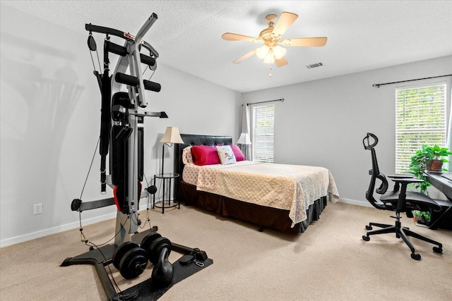 carpeted bedroom with a textured ceiling, visible vents, a ceiling fan, and baseboards