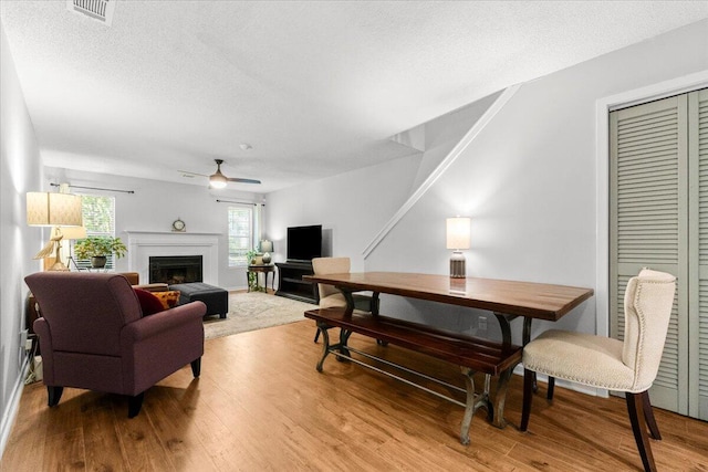 living area with wood finished floors, visible vents, a fireplace, a textured ceiling, and ceiling fan