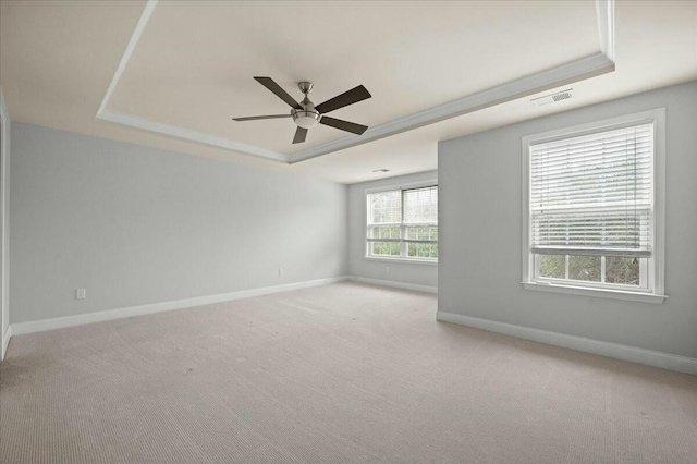 empty room featuring crown molding, ceiling fan, a raised ceiling, and light carpet