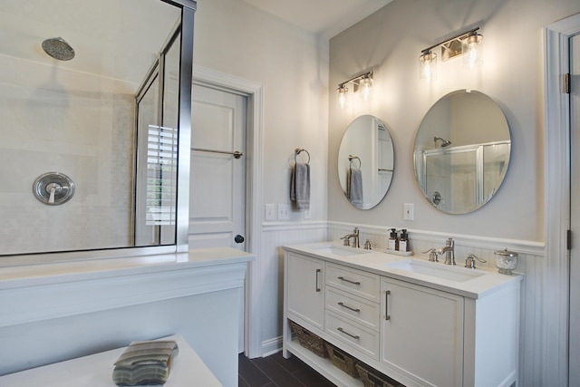 bathroom with a shower with shower door, a wainscoted wall, and double vanity