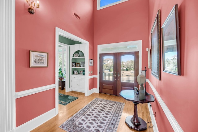 entrance foyer with french doors, light wood finished floors, visible vents, a towering ceiling, and baseboards