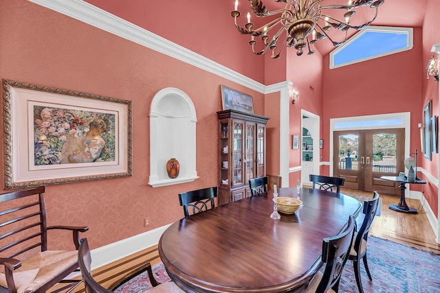 dining area with baseboards, a towering ceiling, wood finished floors, an inviting chandelier, and french doors