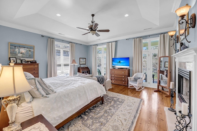 bedroom featuring a fireplace, a raised ceiling, crown molding, and wood finished floors