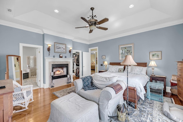 bedroom with light wood finished floors, a tray ceiling, a walk in closet, and a tile fireplace