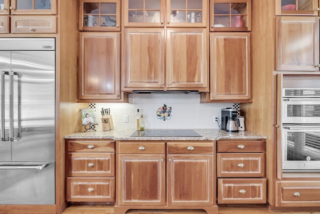 kitchen featuring light stone countertops, glass insert cabinets, stainless steel appliances, and backsplash