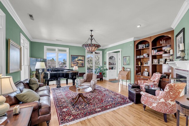 living room with built in shelves, crown molding, a fireplace, visible vents, and wood finished floors