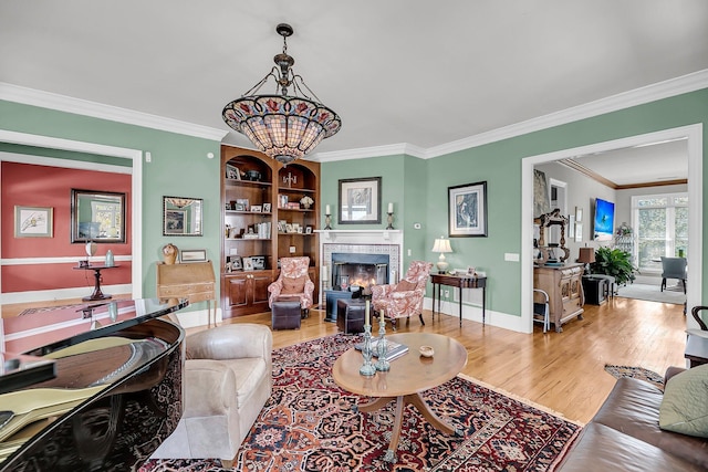 living room featuring baseboards, a tiled fireplace, wood finished floors, crown molding, and a chandelier