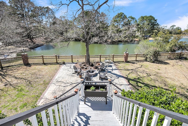 wooden deck with a water view, fence, a fire pit, and a patio