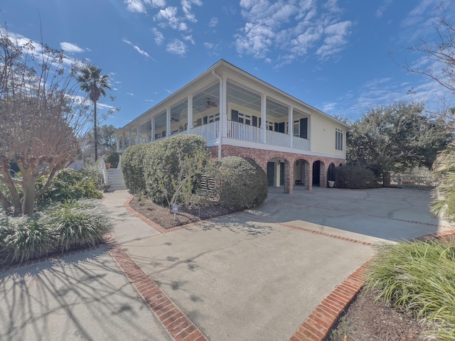 view of front of house featuring driveway, a balcony, a ceiling fan, and brick siding