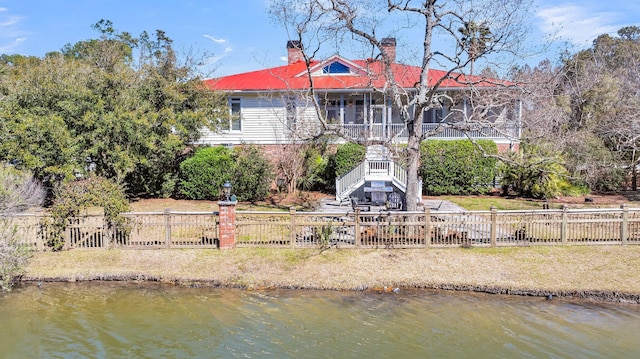 rear view of property with a water view, fence private yard, stairs, and a chimney