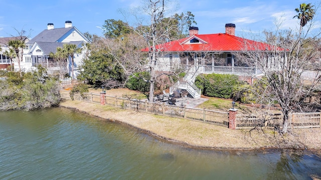 back of house featuring stairway, a chimney, a water view, and a fenced backyard