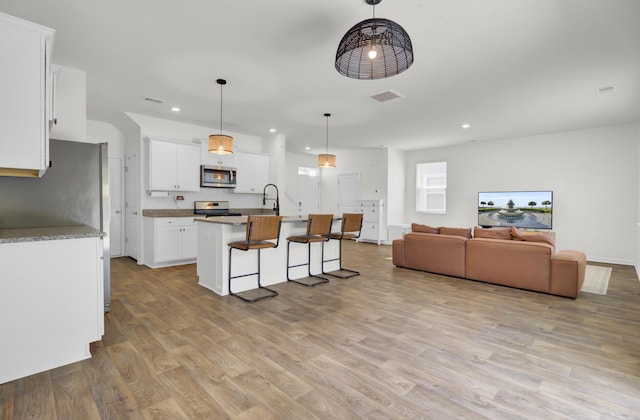 kitchen featuring light wood finished floors, stainless steel appliances, open floor plan, recessed lighting, and white cabinetry
