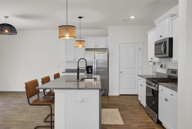 kitchen featuring a kitchen breakfast bar, appliances with stainless steel finishes, a sink, dark wood-style floors, and white cabinetry