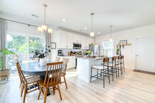 kitchen with light wood finished floors, a kitchen island with sink, white cabinetry, visible vents, and appliances with stainless steel finishes