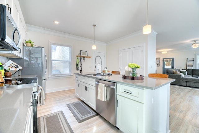 kitchen featuring pendant lighting, light wood finished floors, a sink, stainless steel appliances, and white cabinets