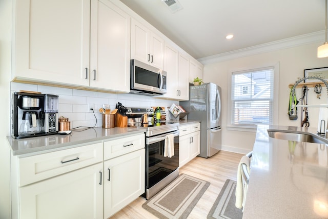 kitchen featuring light wood-style flooring, a sink, crown molding, backsplash, and stainless steel appliances
