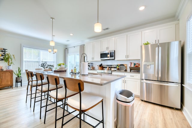 kitchen featuring stainless steel appliances, ornamental molding, light wood-style flooring, a kitchen bar, and white cabinets
