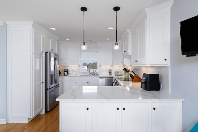 kitchen featuring a peninsula, a sink, white cabinetry, light wood-style floors, and appliances with stainless steel finishes