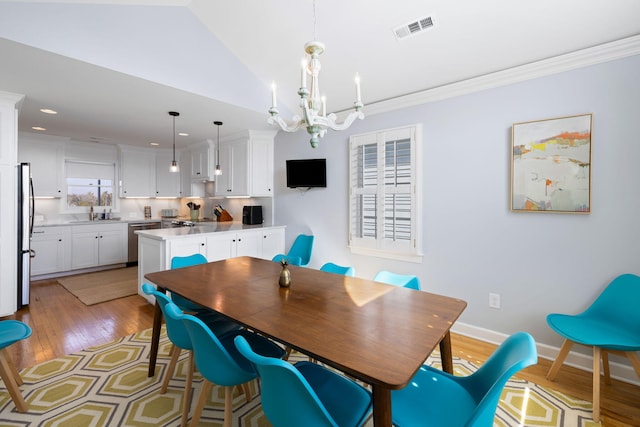 dining room featuring light wood-style floors, baseboards, visible vents, and crown molding