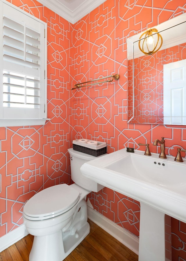 half bathroom featuring toilet, baseboards, crown molding, and wood finished floors