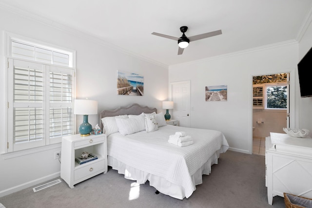 carpeted bedroom with a ceiling fan, visible vents, baseboards, ornamental molding, and ensuite bath