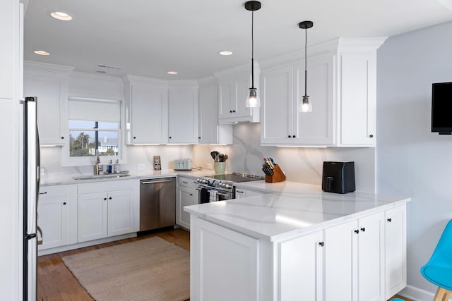 kitchen featuring appliances with stainless steel finishes, white cabinets, a sink, wood finished floors, and a peninsula