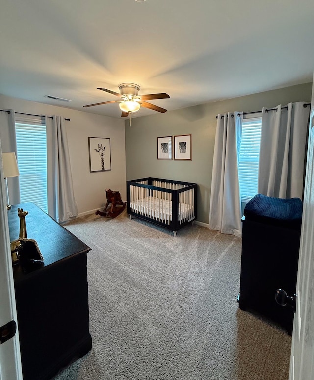 carpeted bedroom featuring ceiling fan and a nursery area