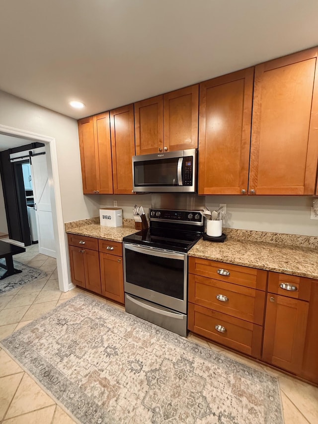 kitchen with light tile patterned flooring, a barn door, light stone counters, and appliances with stainless steel finishes