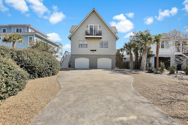 raised beach house with metal roof, an attached garage, a balcony, stairs, and driveway