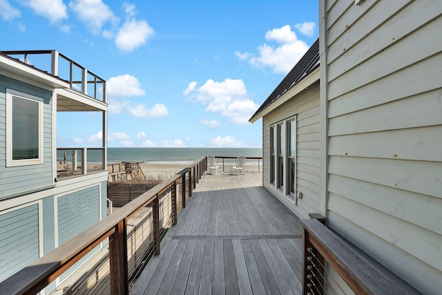 wooden terrace featuring a water view and a beach view