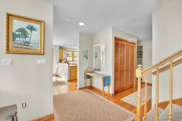 hall with light wood-type flooring, baseboards, stairway, and a textured ceiling