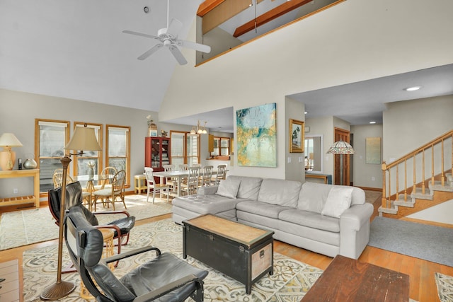 living room featuring stairway, a towering ceiling, wood finished floors, baseboards, and ceiling fan with notable chandelier