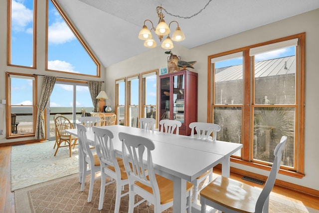 dining space featuring high vaulted ceiling, wood finished floors, visible vents, and an inviting chandelier