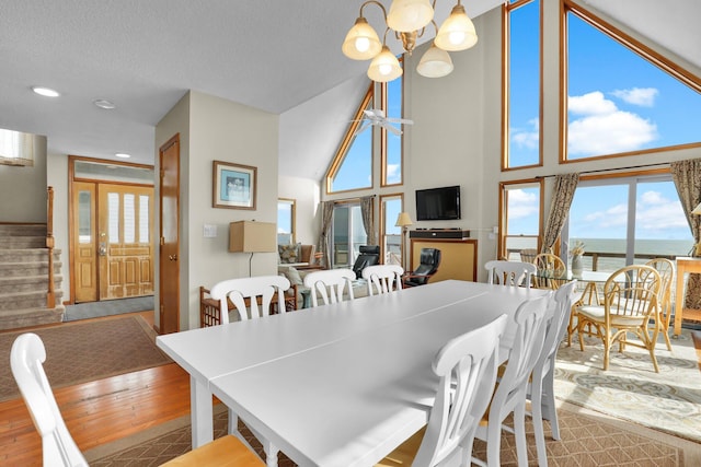 dining room featuring wood finished floors, an inviting chandelier, stairs, a textured ceiling, and high vaulted ceiling