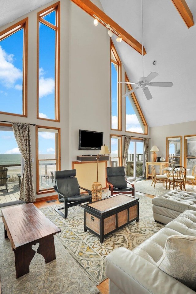 living area with ceiling fan, high vaulted ceiling, beamed ceiling, and wood finished floors