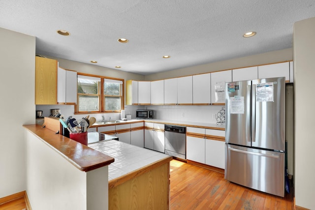 kitchen with appliances with stainless steel finishes, light wood-style flooring, a peninsula, and tasteful backsplash