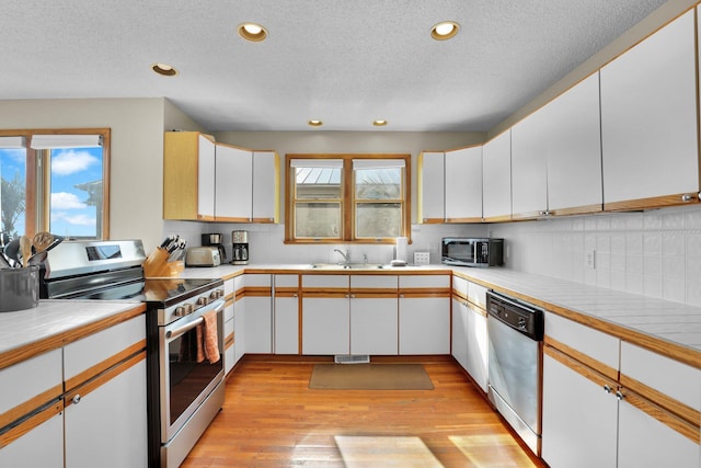 kitchen featuring stainless steel appliances, decorative backsplash, light wood-style flooring, and a healthy amount of sunlight