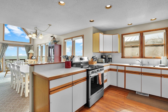 kitchen with a peninsula, visible vents, a healthy amount of sunlight, white cabinetry, and stainless steel electric range