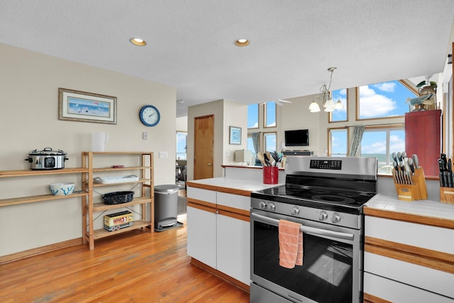 kitchen featuring a notable chandelier, tile countertops, white cabinetry, light wood-type flooring, and stainless steel electric range