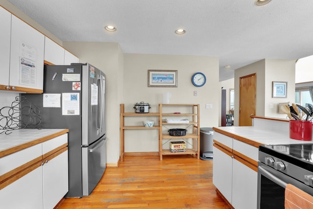 kitchen featuring white cabinets, tile countertops, stainless steel appliances, light wood-type flooring, and recessed lighting