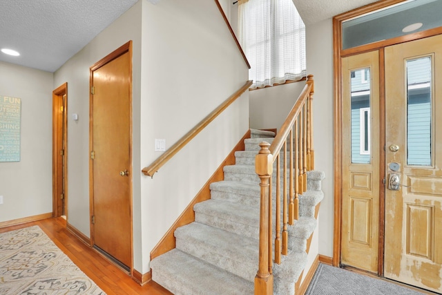 entrance foyer featuring stairs, a textured ceiling, baseboards, and wood finished floors