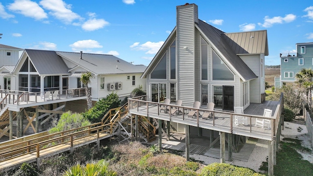 back of property featuring a deck, metal roof, a chimney, and a sunroom