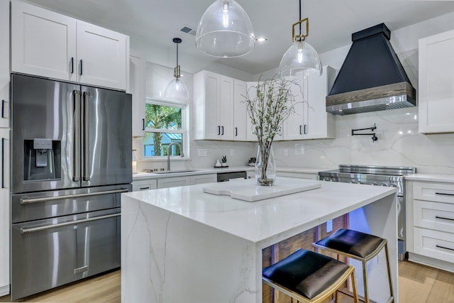 kitchen featuring white cabinets, appliances with stainless steel finishes, a center island, and wall chimney range hood