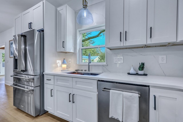 kitchen with decorative light fixtures, stainless steel appliances, white cabinetry, and sink